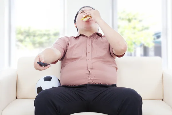 Homem de negócios gordo bebendo cerveja e sentado no sofá para assistir TV — Fotografia de Stock