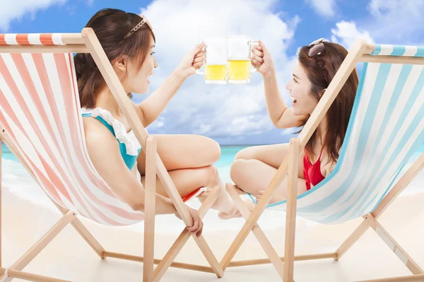 Two sunshine girl holding beer cheers  on a beach chair — Stock Photo, Image