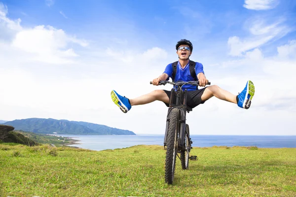 Funny young backpacker riding a bicycle on a meadow — Stock Photo, Image