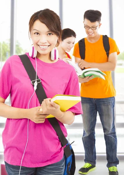 Hübsche junge Studentin hält Bücher und Kopfhörer mit Klassenkameraden — Stockfoto