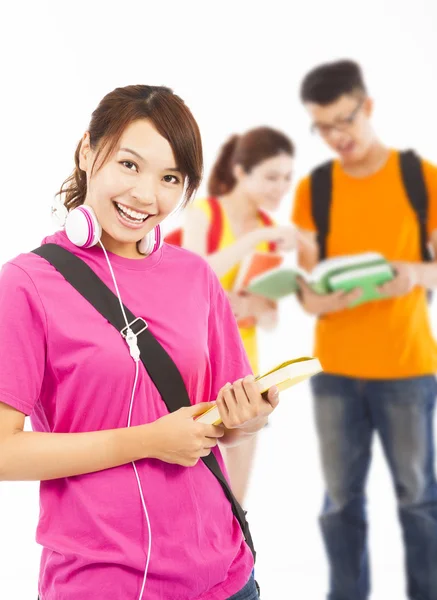 Sonriente joven estudiante sosteniendo libros y auriculares con compañeros de clase — Foto de Stock