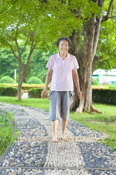 Азиатка постарше, идущая по каменной дорожке — стоковое фото