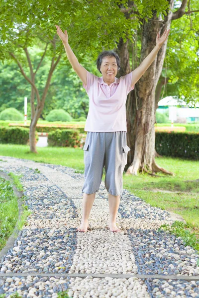 Happy grandmother standing on stone walkway and raise hands — Stock Photo, Image