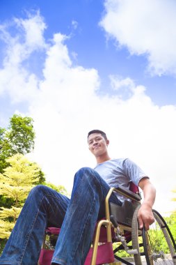  young man sitting on a wheelchair with natural background clipart
