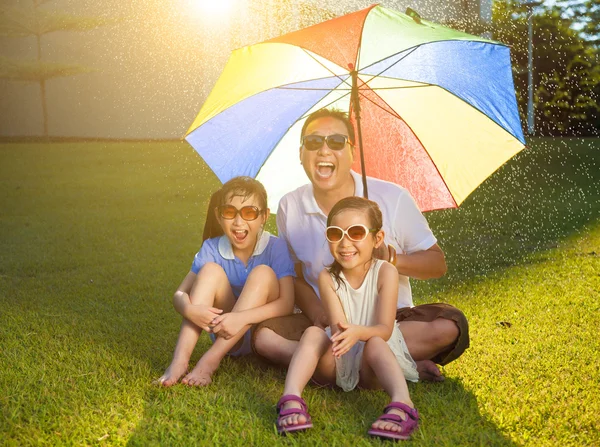 Pai e filhas sentados em um prado com guarda-chuva colorido — Fotografia de Stock