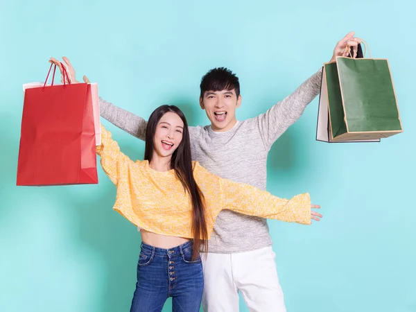 興奮した若いカップル保持ショッピングバッグ 青の背景に隔離 — ストック写真