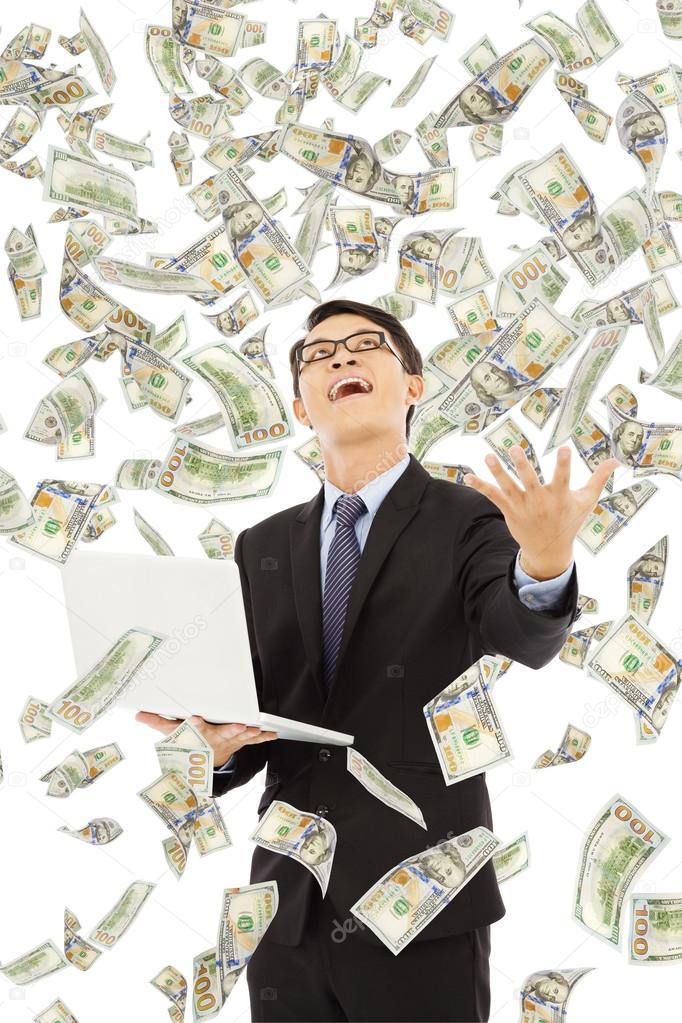 happy business man holding a laptop with money rain