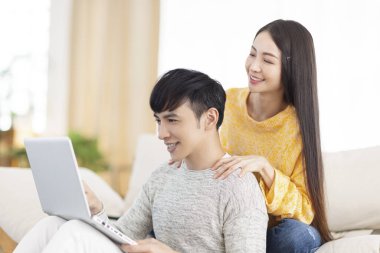 Genç adam kanepede dizüstü bilgisayar kullanarak oturuyor..