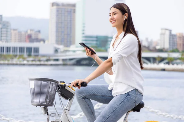 ヘッドフォンで笑顔の女の子 公園でスマートフォンや乗馬自転車を保持します — ストック写真