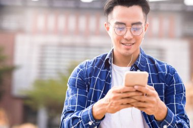 Gülümseyen adam müzik dinliyor ve yürürken cep telefonu kullanıyor. 