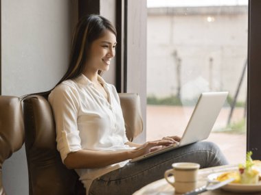 Laptop kullanan ve kahve dükkanında çalışan genç bir kadın.