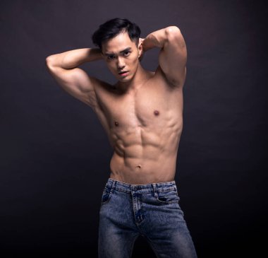 Muscular bodybuilder Asian guy doing posing over black background