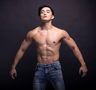Muscular bodybuilder Asian guy doing posing over black background