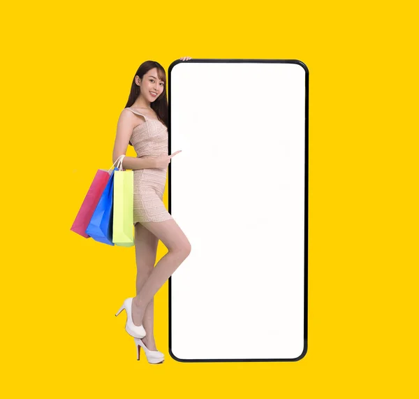 幸せな若い女性が立っていると空白の白い画面で大きなスマートフォンをリース 携帯電話のコンセプトでオンラインショッピングをし — ストック写真