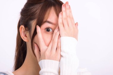 Elleriyle yüzünü örten ve kameraya bakan genç bir kadın.