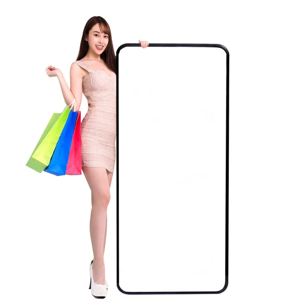 快乐的年轻女子站在那里 依靠着大大的智能手机和空白白屏 使用流动电话概念在网上购物 — 图库照片