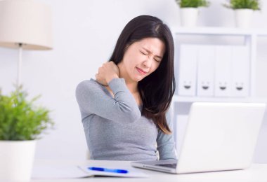  Genç bir kadın dizüstü bilgisayarın önünde oturuyor, boyna dokunuyor ve acı çekiyor.