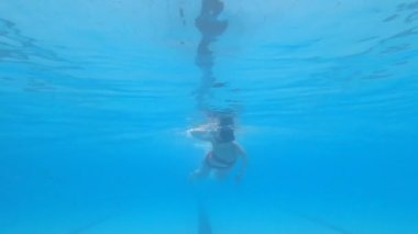 Havuzda yüzen genç bir kadın su altında poz veriyor.