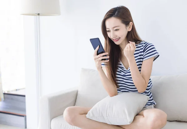 Mujer Joven Emocionada Mirando Teléfono Inteligente Sonriendo Mientras Sienta Sofá — Foto de Stock