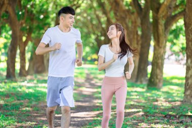 Genç çift güneşli bir günde parkta birlikte koşuyor.