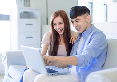  Oturma odasındaki kanepede dinlenen mutlu çift dizüstü bilgisayarla interneti arıyor.