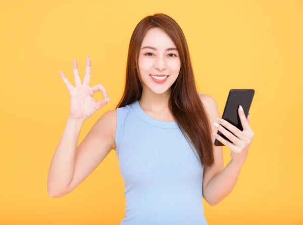 Smiling Asian Woman Holding Mobile Phone Yellow Background Showing Sign — ストック写真