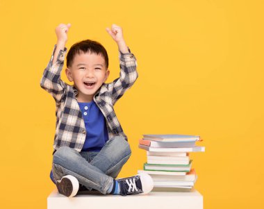  Happy kid sitting with books isolated on yellow background