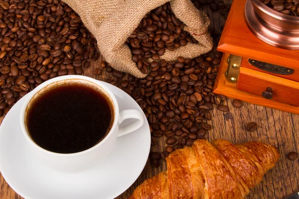 Tasse à café avec un croissant et grains de café frais — Photo