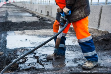Yol işçisi yol yapımı sırasında eski asfaltı kaya matkabıyla temizliyor.
