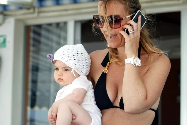 Mãe falando ao telefone com o bebê em seus braços — Fotografia de Stock