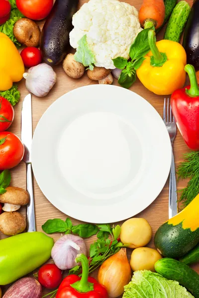 Verduras orgánicas alrededor de la placa blanca con cuchillo y tenedor — Foto de Stock