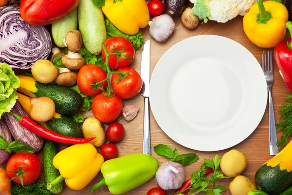 Verduras orgánicas frescas alrededor de la placa blanca con cuchillo y tenedor — Foto de Stock