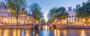 Amsterdam mı? Amsterdam 'ın tarihi şehir merkezinin panorama manzarası. Amsterdam 'ın geleneksel evleri ve köprüleri. Renkli bir akşam ve sudaki ışıkların huzur dolu yansıması. Tarihi bir şehre Avrupa seyahati. Avrupa, Hollanda, Holla