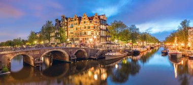Amsterdam, Hollanda. Amsterdam 'ın tarihi şehir merkezinin panoraması. Amsterdam 'ın küçük kasabasının geleneksel evleri ve köprüleri. Romantik bir akşam ve sudaki evlerin parlak bir yansıması. Avrupa 'nın tarihi şehrine seyahat. Avrupa, Alt