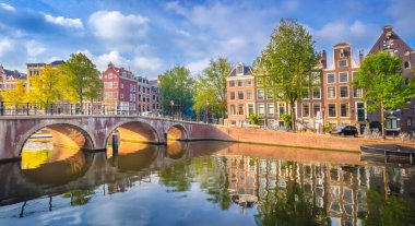 Amsterdam mı? Amsterdam 'ın tarihi şehir merkezinin panoramik manzarası. Amsterdam 'ın geleneksel evleri ve köprüleri. Sabahın erken saatlerinde güneşli bir sabah ve sudaki evlerin huzurlu yansıması. Tarihi bir kasabaya Avrupa seyahati. Avrupa, Hollanda
