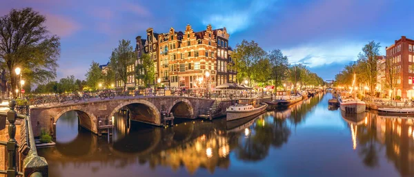 Amsterdam. Panoramic view of the historic city center of Amsterdam. Traditional houses and bridges of Amsterdam town. A romantic evening and a bright reflection of houses in the water. European travel to the historic city. Europe, Netherlands, Hollan