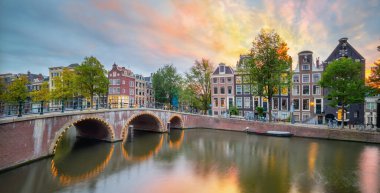 Amsterdam 'da romantik gün batımı. Eski evlerin, köprünün ve kanalın panoramik manzarası. Amsterdam, Hollanda, Hollanda, Avrupa.