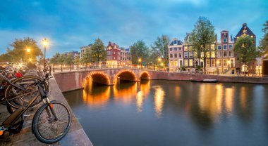 Amsterdam 'da güzel bir akşam. Eski evlerin, bisikletlerin, köprünün ve eski merkezdeki kanalların panoramik manzarası. Şehrin aydınlanması için. Amsterdam, Hollanda, Hollanda, Avrupa