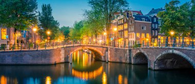 Romantik Amsterdam ışıkları yaktı. Fener ışıkları, köprüler, kanallar ve şirin Hollanda evleriyle ünlü tarihi merkezin akşam manzarası. Amsterdam, Hollanda, Avrupa seyahati. Panoramik