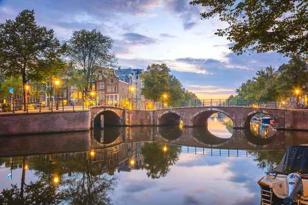 Romantic Amsterdam.  Famous view of Amsterdam at dawn. Downtownr. The lanterns are still on, but the sun has already colored the sky in multi-colored. Picturesque quiet morning. Reflections in the water. Bridges, canals and houses. Holland, Europe