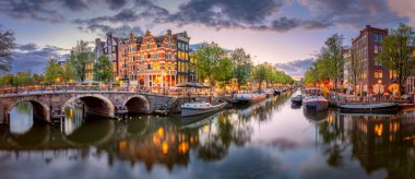 Amsterdam mı? Amsterdam şehir merkezinin panoramik manzarası. Amsterdam 'ın geleneksel evleri ve köprüleri. Mavi bir akşam ve sudaki ışıkların huzur dolu yansıması. Uzun pozlama. Tarihi bir şehre Avrupa seyahati. Avrupa, Hollanda, Holl