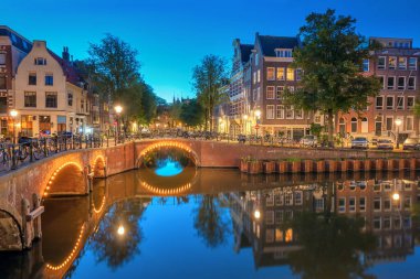Amsterdam mı? Amsterdam 'da sabahın erken saatlerinde. Şafaktan önce mavi alacakaranlık. Tipik eski evler ve köprüler, aydınlanma. Suda yansıma. Amsterdam, Hollanda, Hollanda