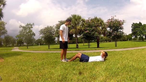 Young man doing sit-ups, exercising with personal trainer — Stock Video