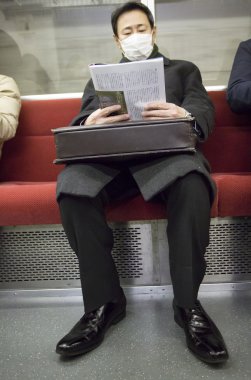 Man reading his newspapper in the Tokyo metro clipart
