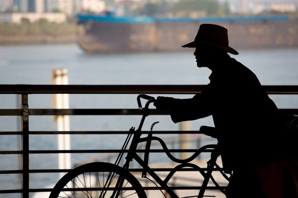 Man pushing his bicycle with the river and a boat — Stock Photo, Image