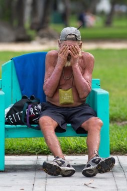 Unrecognizable homeless in Miami Beach sitting on a bench clipart