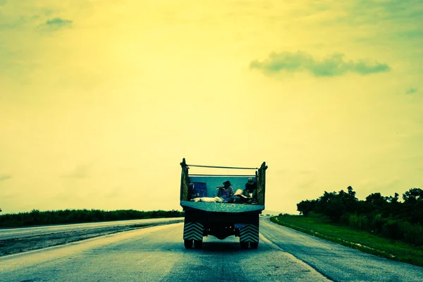 Two people traveling in back of a truck on an empty road in Cuba — Stock Photo, Image