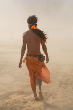 Turuncu kumaş ile giyinmiş bir kum fırtınası'nda yürüyüş hippi adam