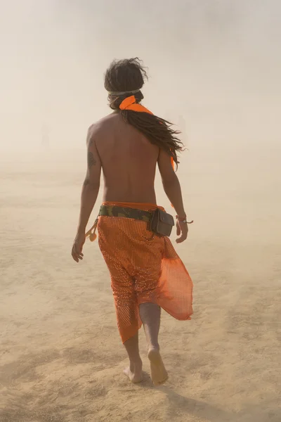 Hippie homem andando em uma tempestade de areia vestida com tecidos laranja — Fotografia de Stock