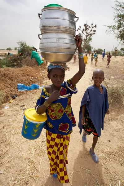 Afrikanische Kinder spazieren auf dem Land, ein junges Mädchen trägt — Stockfoto